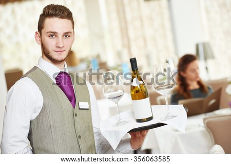 Waiter occupation. Young man with wine bottle and glasses on tray servicing in restaurant