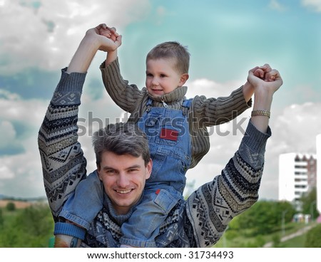 Little joyful boy sitting on the young man shoulders outdoors