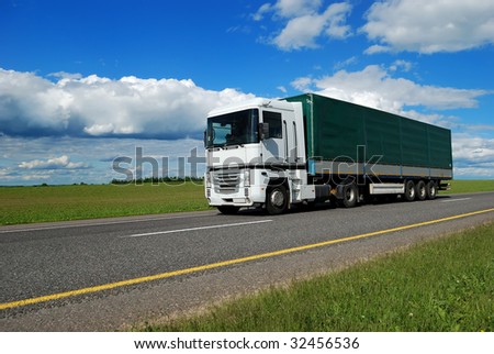 white lorry with green trailer on the highway over blue cloudy sky