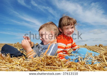 Smiling Boy and girl sitting back-to-back on the straw outdoors over blue sky