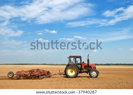 Agriculture tractor in yellow field outdoors in summer with plough