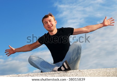 young happy man with wide open arms welcoming outdoors over blue sky