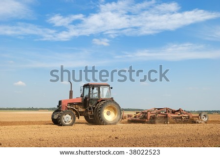 Agriculture tractor in yellow field outdoors in summer with plough