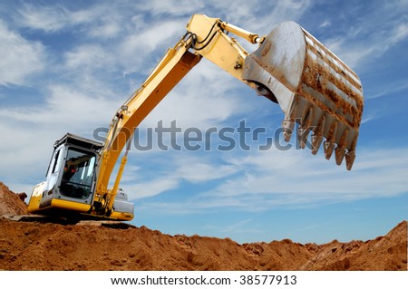 Excavator standing in sandpit with raised bucket over cloudscape sky Excavator standing in sandpit with raised bucket over cloudscape sky