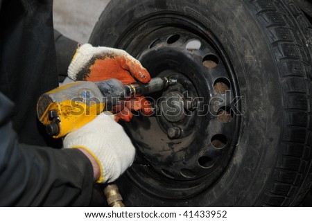 two hands making tyre fitting with air compressed wrench (screwing up bolts)