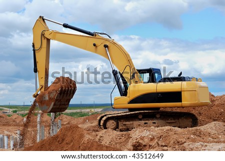 Excavator loader at construction site with sand in bucket over cloudscape sky