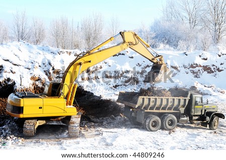 Excavator loading dump truck tipper at open cast over blue sky in winter