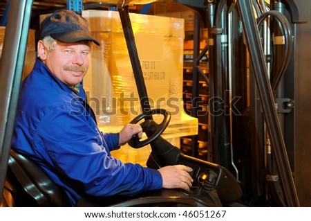 Worker driver of a forklift loader in blue workwear at warehouse