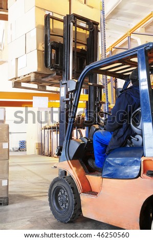 Worker driver of a forklift loader at warehouse loading cardboard boxes on pallet to shelves