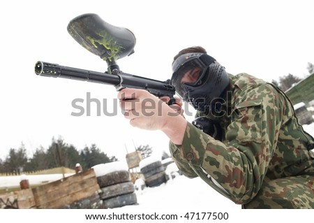 paintball sport player with mask aiming gun and shooting to enemy in winter