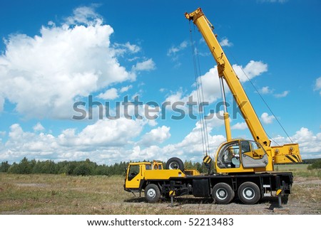 yellow automobile crane with risen telescopic boom outdoors over blue sky