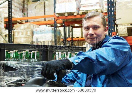 Worker driver of a forklift loader in blue workwear at warehouse