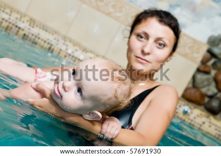 Mother and baby child playing in a swimming pool. Focus on baby face with mother defocused in the background.