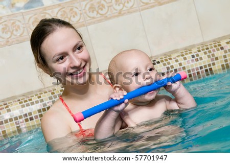 Mother and baby child in a swimming pool. Focus on baby face with mother defocused in the background.