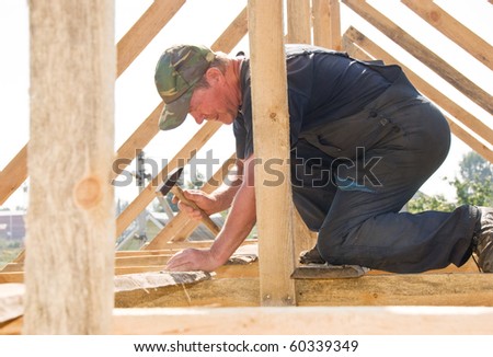 builder worker nailing with hammer at roofing construction works