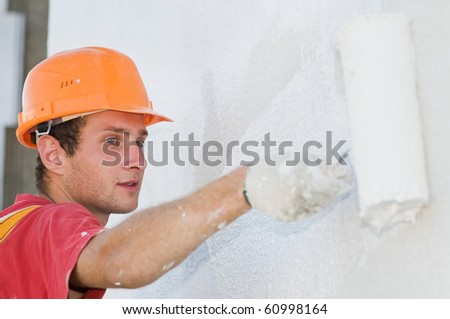 builder worker painting facade of high-rise building with roller