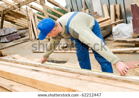 builder worker at roofing works measuring length of wood timber with measuring tape