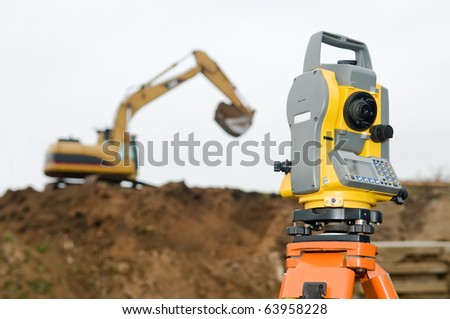 Surveyor equipment theodolite on tripod at building area in front of working construction machinery loader