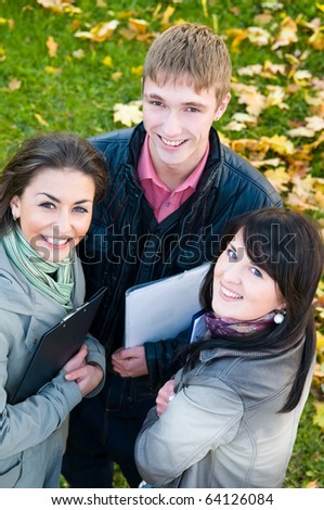 Three students standing with clipboards in park on yellow autumn leaves/ Upper point of view