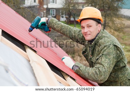 builder worker at roofing works on metal tiling with screwdriver