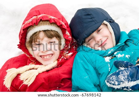 two little children boy and girl lying and laughing at winter outdoors