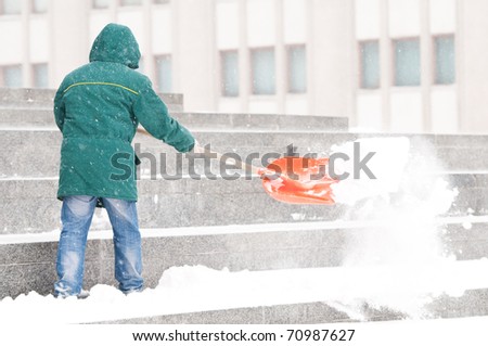 communal services worker in uniform shoveling snow in winter snowstorm