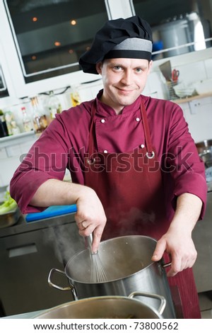 cheerful chef with whisk making sauce in big kitchen pot
