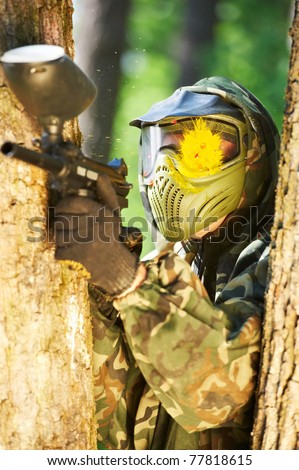 paintball sport player wearing protective mask aiming gun with head shot by paint spot
