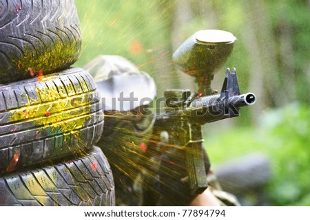 paintball sport player wearing protective mask aiming gun from shelter under gunfire attack with paint splash