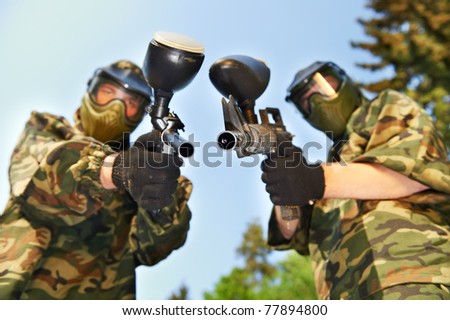two paintball players in protective clothing aiming guns outdoors