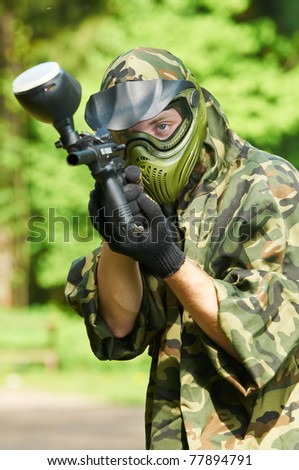 paintball sport player in protective uniform and mask aiming gun before shooting in summer