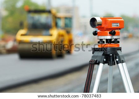Construction surveyor equipment theodolite level tool during asphalt paving works with compactor roller at background