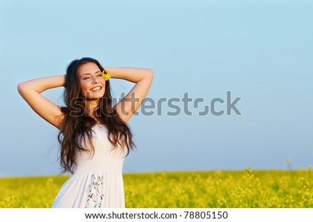 Happy smiling young woman with hands behind head over yellow green rapeseed meadow