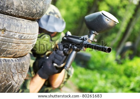 paintball sport player in protective uniform and mask aiming and shooting with gun outdoors