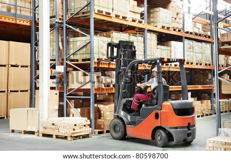 warehouse worker driver in uniform loading cardboard boxes by forklift stacker loader