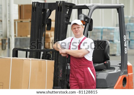 young cheerful warehouse worker driver in uniform in front of forklift stacker loader