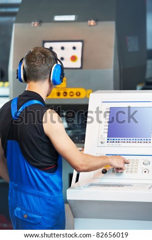 worker at workshop operating punch press machine tool by computer