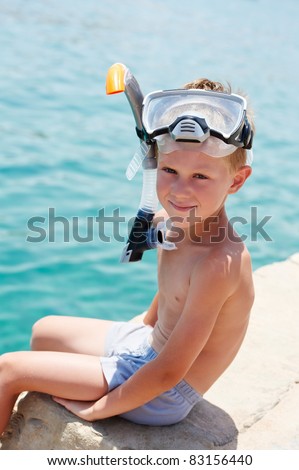 one little smiling boy sitting on pier near red sea with snorkeling gear on
