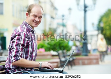 Smiling man with laptop notebook sitting on bench in the street