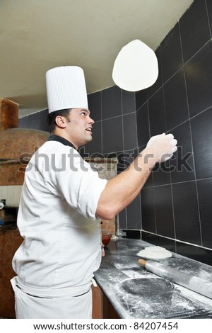 One chef baker in white uniform juggling with bakery pastry for pizza at kitchen