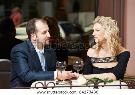 Man and girl drinking wine at street cafe on a date with flower on table