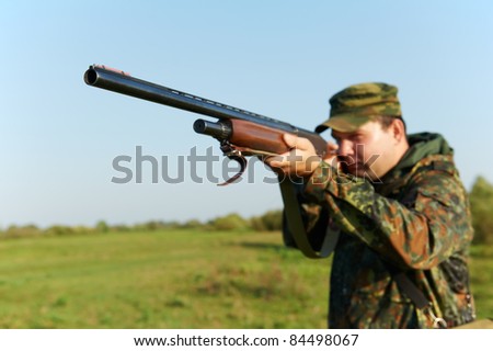 Male hunter in camouflage clothes on the field aiming the hunting rifle during a hunt.