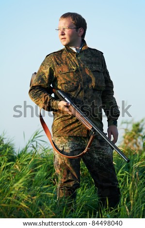 Male hunter in camouflage clothes ready to hunt at lake bank with hunting rifle