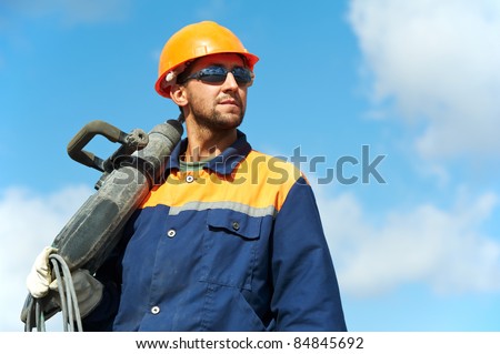 Portarait of positive Builder worker with pneumatic hammer drill equipment over blue sky