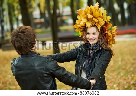 Two young people join hands in park at autumn outdoors date. Girl wear chaplet from maple