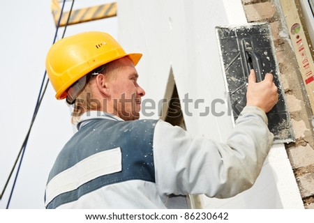 Plaster facade builder worker with roller at thermal insulation works