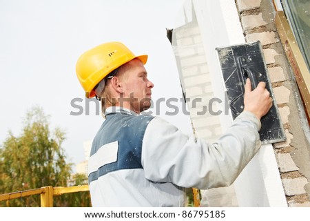 Plasterer facade builder worker with scratching tool at thermal insulation works