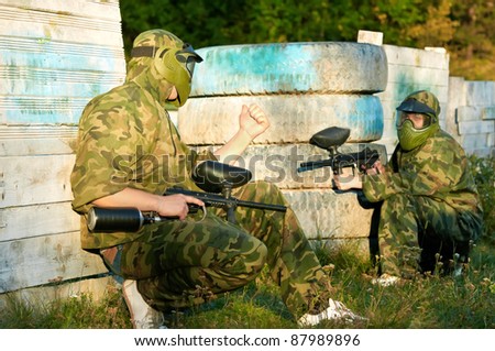 Two paintball sport players in prootective uniform and mask aiming and shoting with gun outdoors