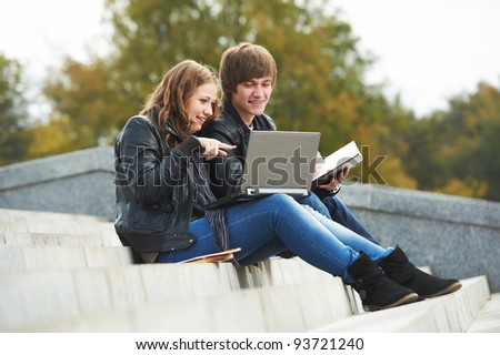 Two students studying with computer notebook outdoors