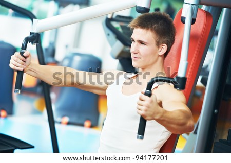 smiling fitness man at chest pectoral muscles exercises with training weight machine station in gym